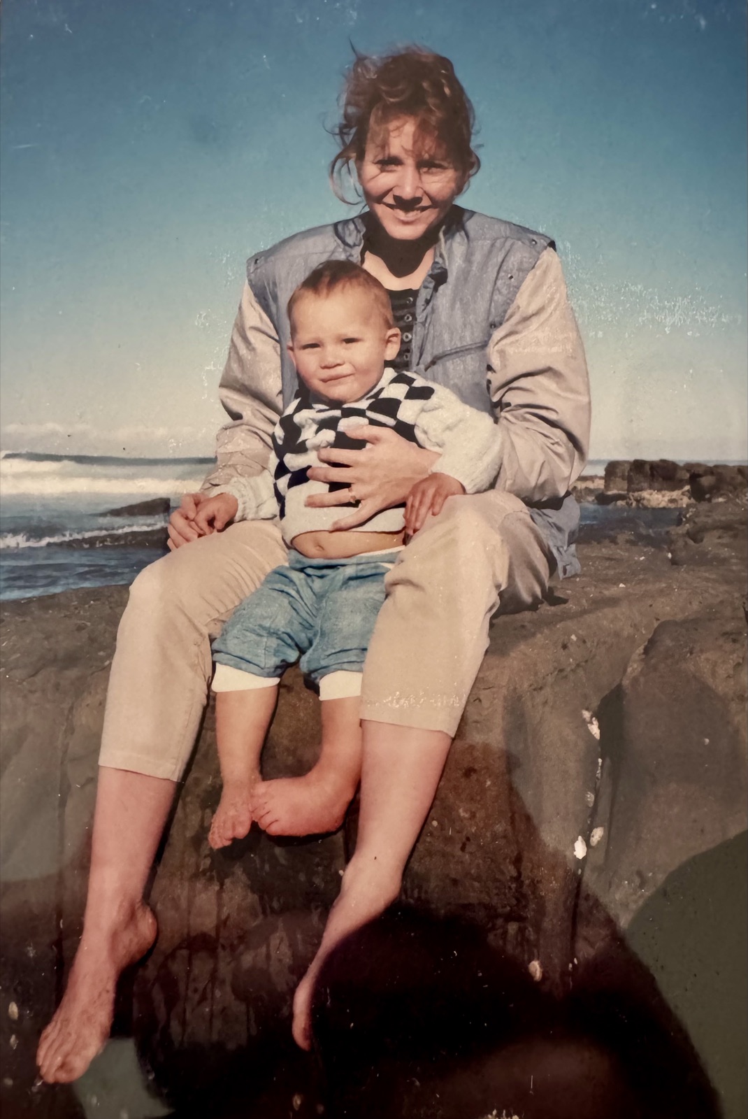 Anne sitting on the rocks by the sea with her toddler on her lap